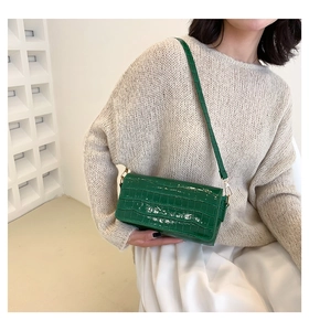 Detail view of green crocodile pattern leather baguette shoulder bag with golden metal hooks