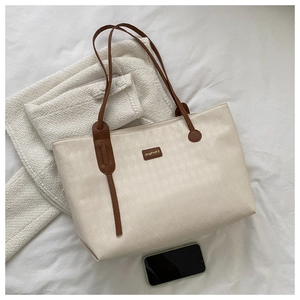 Detailed close-up of beige woven tote bag with brown handles and elegant branding