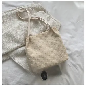 Détail d'un cabas tressé beige montrant la texture carrée et les fines bandoulières
