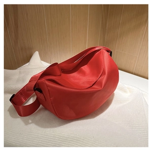 Detail view of red nylon crossbody bag with adjustable strap on a white fabric surface