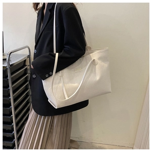 Detail showing cream woven texture tote bag and gold logo plate on a shoulder bag