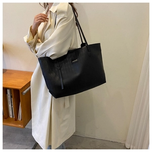 Detail of black leather tote bag featuring refined woven texture and metal logo