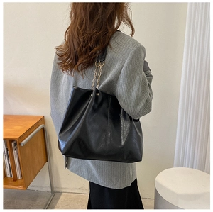 Détail d'un grand sac fourre-tout noir avec bandoulière chaîne dorée à l'épaule