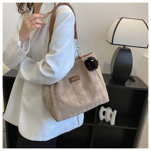 Detail of beige quilted tote bag featuring a leather Fashion tag and black plush pompom