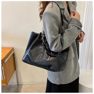 Grand sac cabas en cuir souple noir avec chaîne dorée porté par un mannequin élégant