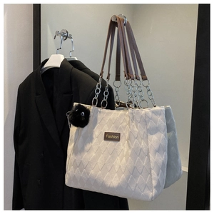 Close-up of white quilted tote bag featuring metal chain strap and fashion label detail