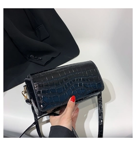 Detail of glossy black crocodile embossed faux leather handbag with gold metal clasp