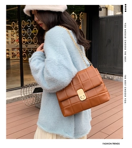 Detail of a brown quilted leather shoulder bag featuring a gold chain strap and metal lock