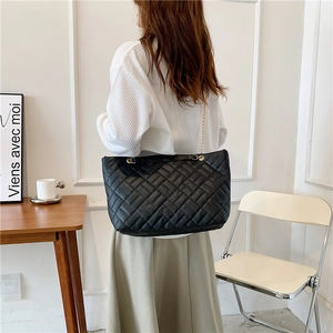 Borsa tote nera trapuntata con catena dorata indossata da modella in un interno moderno