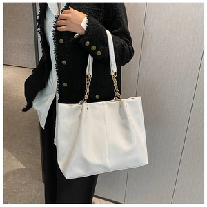 Détail d'un sac cabas blanc en cuir souple avec chaîne dorée porté sur une tenue noire