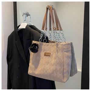 Close-up of beige quilted tote bag with chain strap, fashion label, and black pompom detail