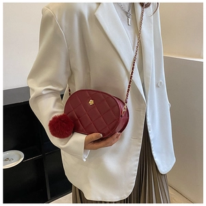 Detail of burgundy quilted oval bag with gold flower logo and red faux fur pompom charm