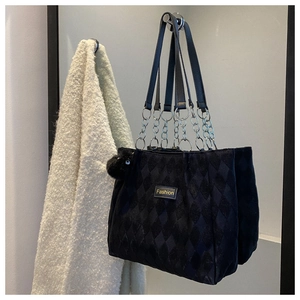 Detail of black quilted velvet tote bag with metal chain handle and plush charm