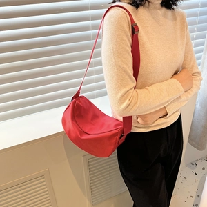 Fashionable red nylon crescent crossbody bag styled with a minimalist knit sweater