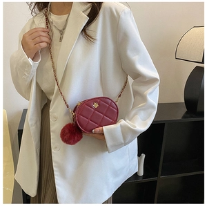 Burgundy quilted oval crossbody bag with gold chain strap and red pompom charm detail