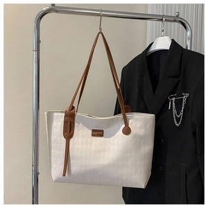 Detail of white quilted tote bag with brown leather straps and metallic logo plate