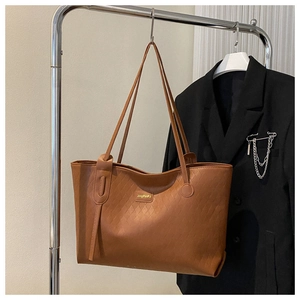 Detail of a brown tote bag featuring textured woven pattern and sleek shoulder straps