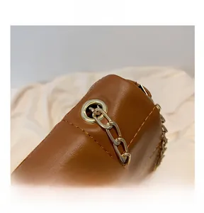 Detail of golden metal eyelets and chain on brown textured leather crossbody bag