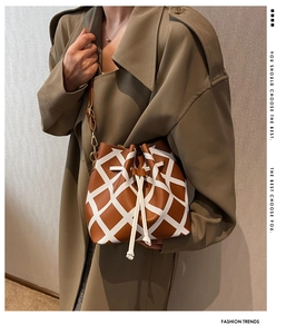 Brown and white plaid drawstring bucket bag with leather strap shown on model's shoulder