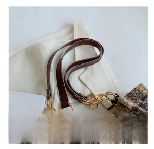 Détail d'une bandoulière en cuir marron et chaîne dorée sur un sac cabas à carreaux