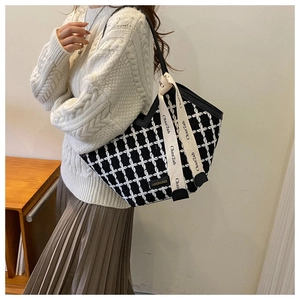 Detail of checkered tote bag with woven straps and fashion labels in casual style