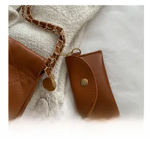 Detail of a brown leather mini pouch charm on a quilted tote bag with gold chain strap