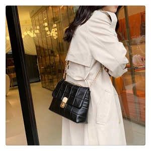Close-up of black quilted chain bag with gold buckle on a beige trench coat