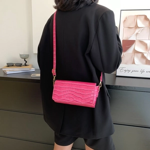 Hot pink croco embossed baguette shoulder bag with gold hardware worn on black suit