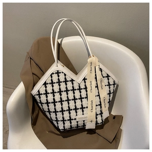 Close-up of black and white plaid tweed tote bag with leather straps and decorative ribbon