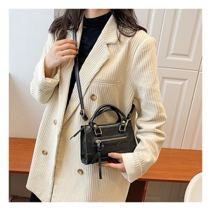 Borsa a mano nera con nappe indossata da modella con giacca in velluto beige