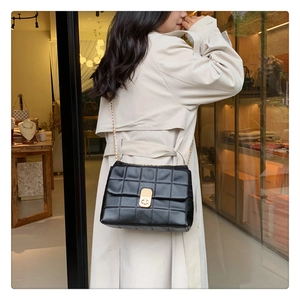 Detail of black quilted chain bag with gold buckle on a model in a boutique