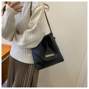 Close-up of black quilted bucket bag with gold chain strap worn by a model