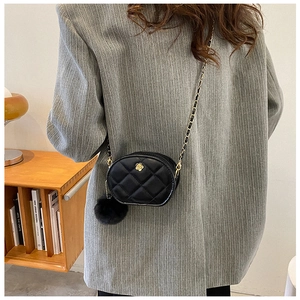 Quilted crossbody chain bag with gold floral buckle and plush charm shown in a cozy room