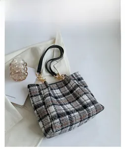 Détail d'un sac cabas en tweed à carreaux avec bandoulière en chaîne sur fond minimaliste