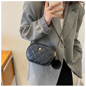 Detail of black quilted oval crossbody bag with gold floral accent and plush ball charm