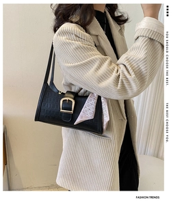 Detail of black crocodile texture shoulder bag with gold buckle and decorative silk scarf