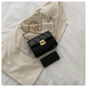 Detail of a black quilted chain bag with gold buckle on a beige blazer background