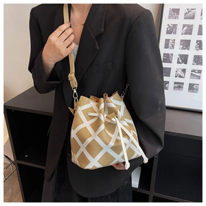 Detail of khaki quilted bucket bag with white drawstring closure and leather strap