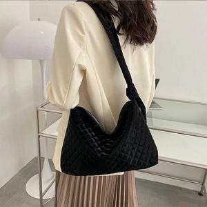 Lifestyle shot of woman wearing black quilted shoulder bag with decorative knotted strap