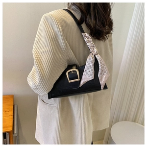 Detail of black crocodile pattern shoulder bag with silk scarf and gold buckle on blazer