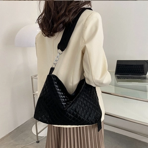 Detail of black quilted velvet hobo bag with silver chain and wide strap on office model