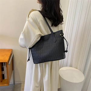 Large black quilted tote bag with drawstring detail carried by a model in a trench coat