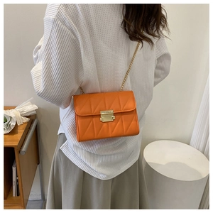 Detail of orange quilted crossbody bag with golden chain and metallic lock on model