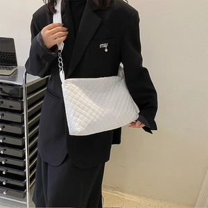 Detailed view of a white quilted crossbody bag with wide shoulder strap and silver chain link