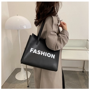Model wearing black leather tote bag with white FASHION print in minimalist interior