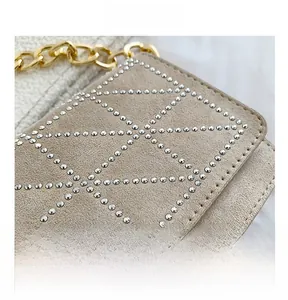 Detail showing khaki suede texture with silver rivet studs and a gold chain strap