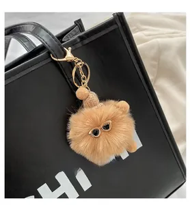 Close-up of fluffy brown pompom charm with mini glasses and hat on black tote bag