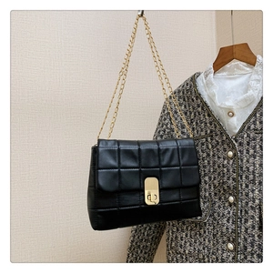 Detail of black quilted leather shoulder bag with gold chain strap and metal turn-lock closure