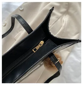 Detail shot of smooth gold-tone zipper closure on the black faux leather tote bag