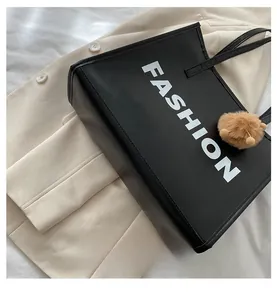 Detail of black tote bag with white FASHION print and brown faux fur pompom keychain